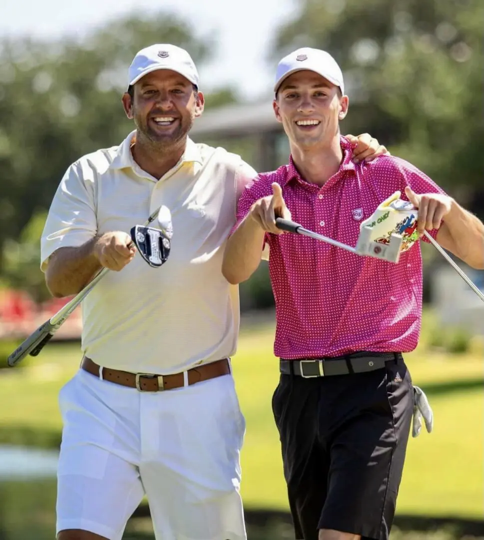 Two men standing next to each other holding golf clubs.